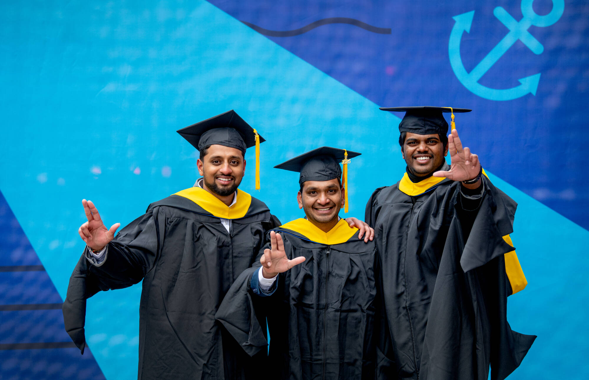 3 graduate students at commencement showing the anchors up sign for GVSU lakers